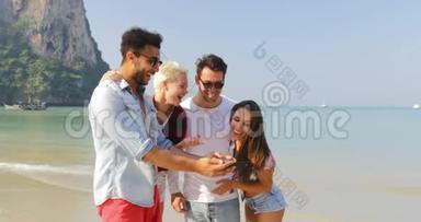 人们在海滩上使用手机观看照片两对情侣在度假时拥抱快乐的男女游客